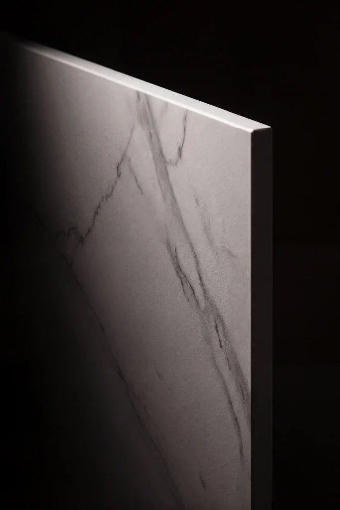 A detailed close-up portrait of a sintered stone slab surface, lit from above to reveal the dense mineral character, subtle Calacatta-style marble veining visible against a dark background.